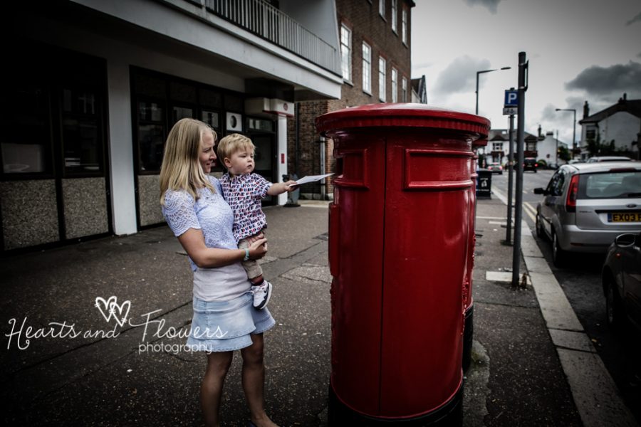 A mummy holds her little boy up so he can reach the postbox.