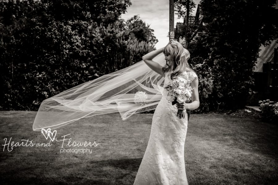 bride is standing in the garden with her veil blowing in the wind