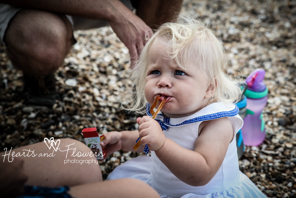 a little girl is eating chewy sweets on the beach